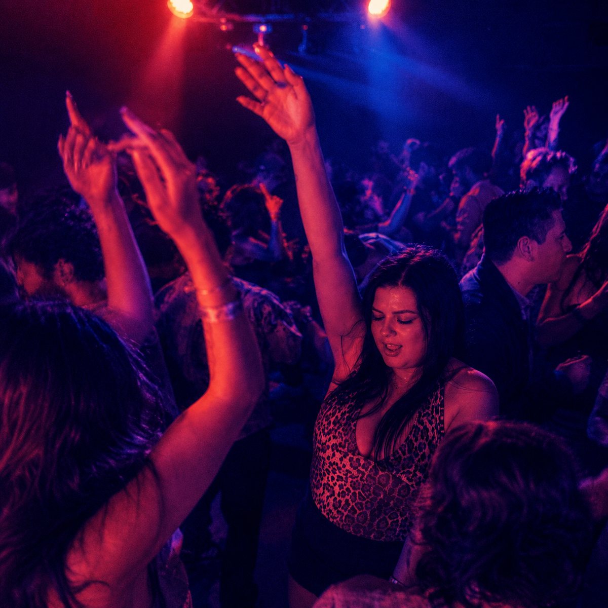Hands raised on a packed dancefloor under red and blue stage lights