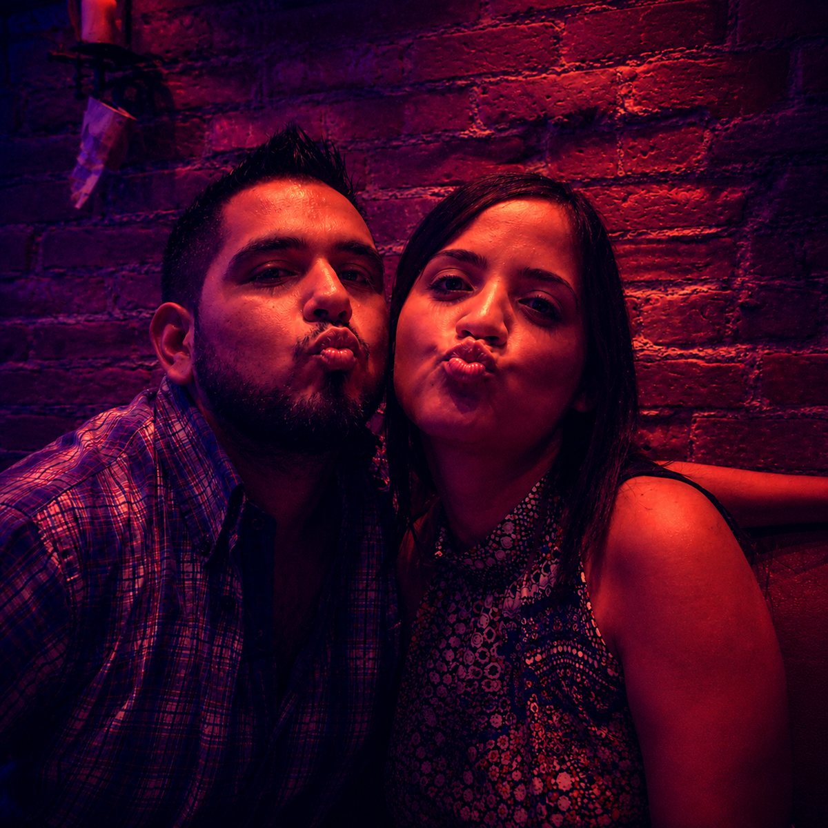 Two people leaning in close against a warm magenta brick wall